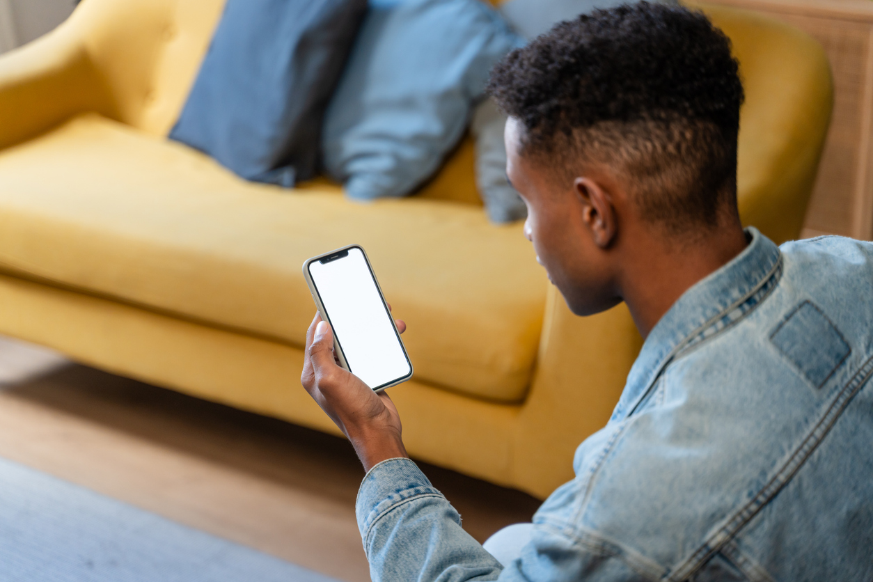 side view of african american man holding smartphone with blank screen at home